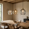Drie glazen hanglampen boven een houten eettafel in een warm, natuurlijk interieur
